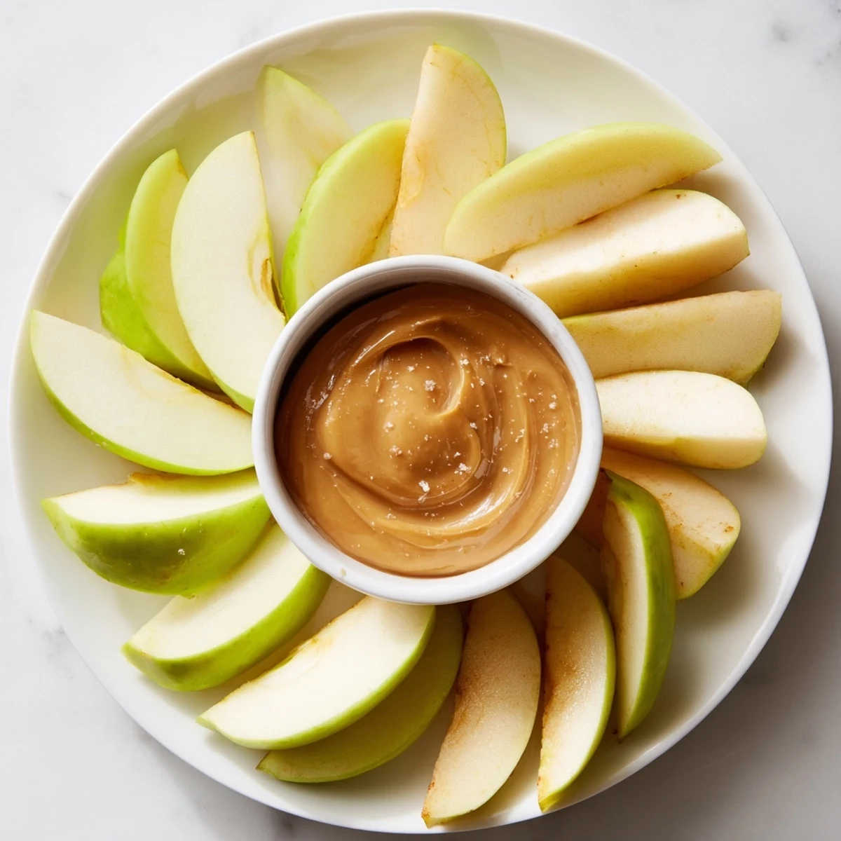 Fresh apple slices radiate around a bowl of luscious caramel dip, perfect for dipping.