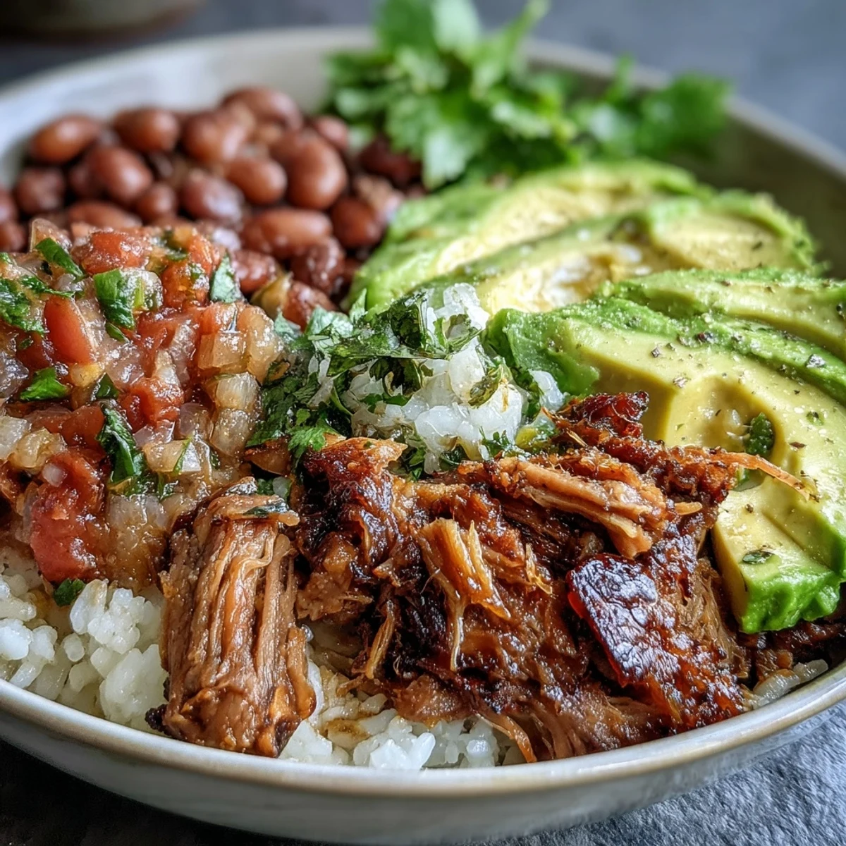 A hearty Carnitas Bowl with fluffy rice, tender slow-cooked pork, creamy avocado, and fresh pico de gallo.