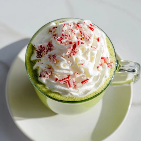 A vibrant mug of Cozy Peppermint Matcha Christmas Latte topped with sweet, fluffy whipped cream.