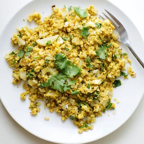 Golden turmeric cauliflower rice sizzling in a skillet with chopped onion, garlic, and fresh cilantro garnish.