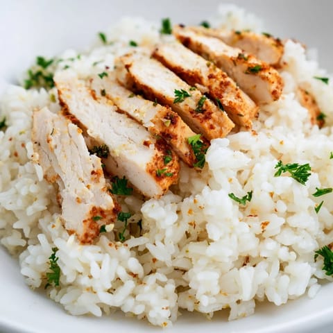 A close-up view of juicy grilled chicken breast and fragrant, buttery rice with minced garlic and herbs in a warm, inviting bowl.