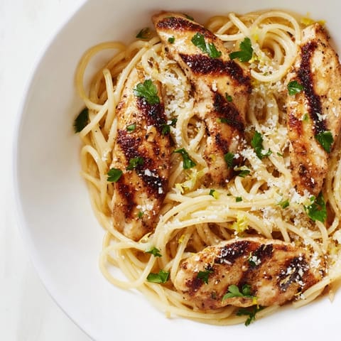 Close-up of Brown Butter Lemon Chicken Pasta showing glossy sauce clinging to al dente spaghetti, with lemon wedges and fresh herbs on the side.  