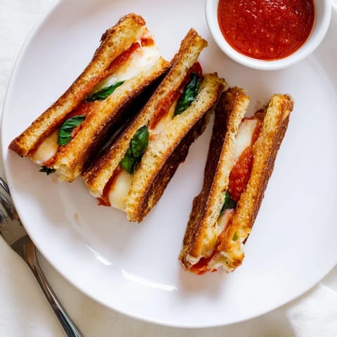 Golden, melty Caprese Grilled Cheese Dippers with melted mozzarella, fresh basil, and ripe tomatoes beside a bowl of marinara for dipping.