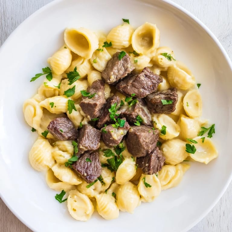 A close-up of tender, flavorful garlic butter steak bites nestled over warm, golden cheesy pasta.
