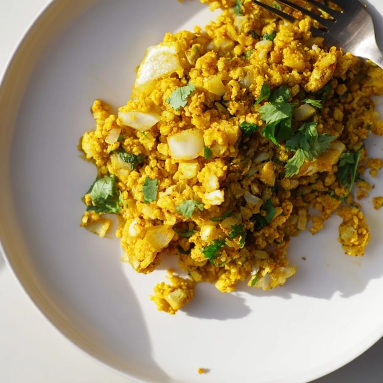 Vibrant turmeric cauliflower rice served warm as a side dish, topped with fresh parsley and lemon.