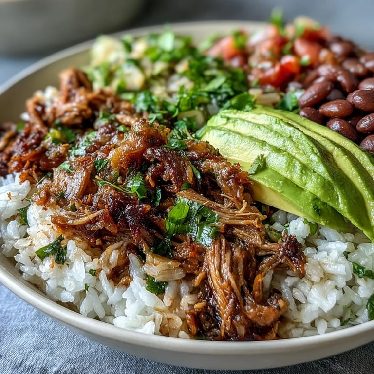 Close-up of a vibrant Carnitas Bowl featuring shredded carnitas, beans, rice, and zesty lime wedges.