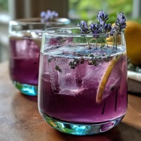 A vibrant lavender lemonade spritz with floral syrup, fresh lemon, and sparkling wine served over ice.